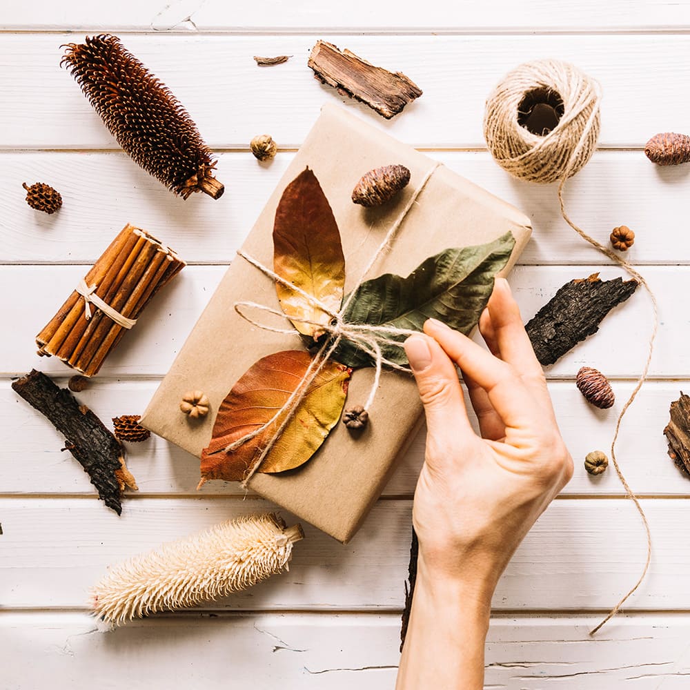 Una mano haciendo un nudo en un regalo hecho por tela papel tijeras, con materiales naturales del bosque.
